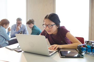 Girl student using laptop while assembling robot