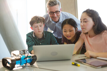 Obraz premium Male teacher and students using laptop in classroom