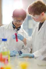 Boy students examining liquid in test tube, conducting scientific experiment in laboratory classroom