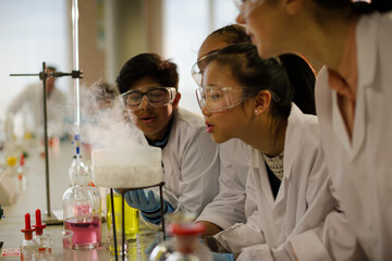 Female teacher and students watching scientific experiment chemical reaction in laboratory classroom