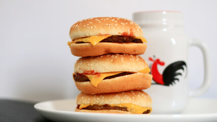 Pile of cheeseburgers and a cup of drink on white background.