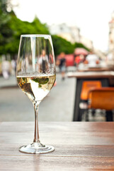 Glass of white wine close up. Alcoholic drink on a wooden table on a background of the city. Transparent wine on the summer terrace of the restaurant.