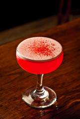 Red cocktail on bar counter. Drink with martini, gin, rum, tequila and fruit on the background of bottles with alcohol. Glass with booze on a wooden board.