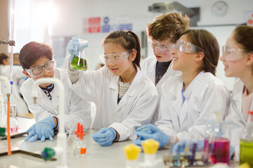 Curious students conducting scientific experiment, examining liquid in beaker in laboratory classroom