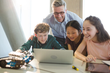 Male teacher and students using laptop in classroom