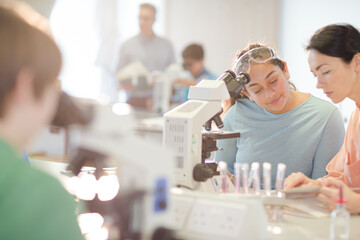 Female teacher and girl student conducting scientific experiment at microscope in laboratory classroom