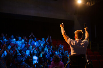 Female speaker in wheelchair on stage waving to audience