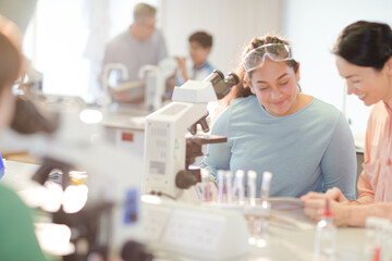 Fototapeta na wymiar Female teacher and girl student conducting scientific experiment at microscope in laboratory classroom