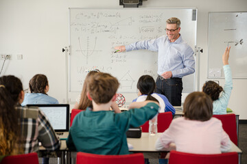Male teacher leading lesson at whiteboard in classroom
