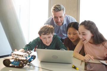 Male teacher and students using laptop in classroom