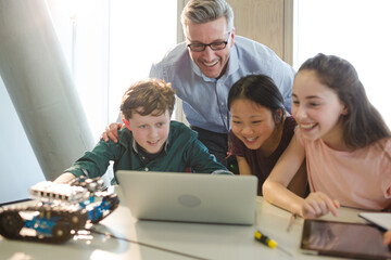 Male teacher and students using laptop in classroom