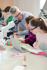 Male teacher and girl students conducting scientific experiment at microscope and laptop in laboratory classroom