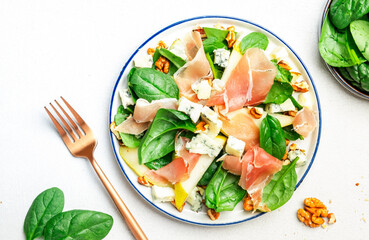 Pear salad with prosciutto, blue cheese, spinach, walnuts on white background, top view, copy space