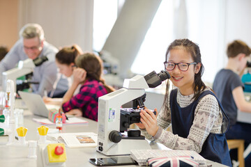Portrait smiling, confident girl student using microscope, conducting scientific experiment in laboratory classroom