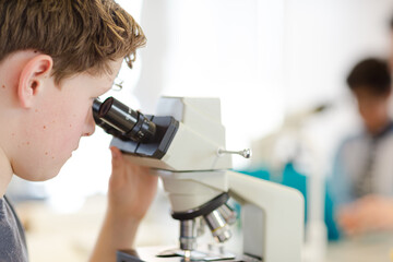 Boy student conducting scientific experiment at microscope and computer in laboratory classroom