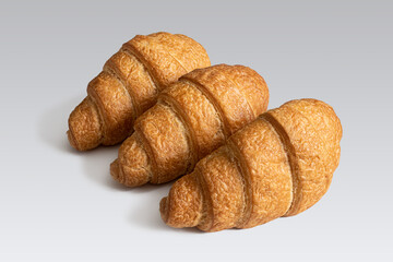Three fresh croissants made of puff pastry on a light gray background