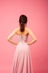 back view of woman in delicate pink corset dress with lacing and lace, isolated on pink background. 