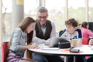 Male teacher and students using laptop at table