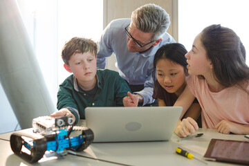Male teacher and students using laptop in classroom