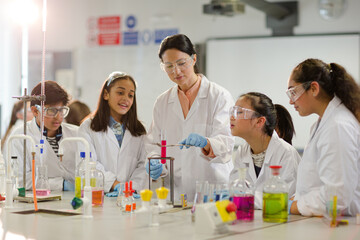 Female teacher and students conducting scientific experiment, watching liquid in test tube in laboratory classroom