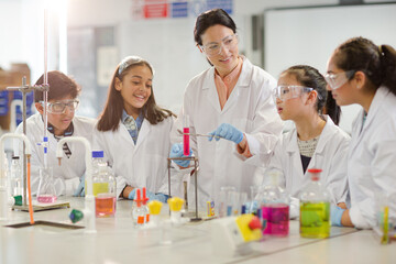 Female teacher and students conducting scientific experiment, watching liquid in test tube in...