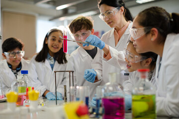 Female teacher and students conducting scientific experiment, watching liquid in test tube in...