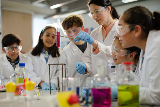 Female teacher and students conducting scientific experiment, watching liquid in test tube in laboratory classroom