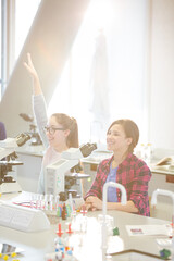 Eager girl students raising arms behind microscopes in laboratory classroom