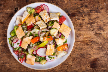 Fattoush salad with vegetables and pita in a plate on the table, top view, copy space for recipe