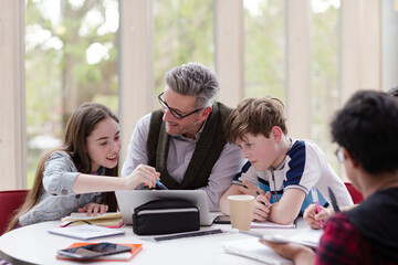 Obraz premium Male teacher and students using laptop at table