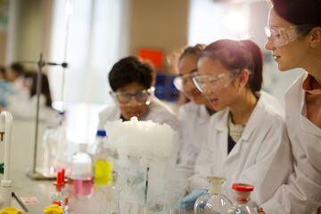 Female teacher and students watching scientific experiment chemical reaction in laboratory classroom