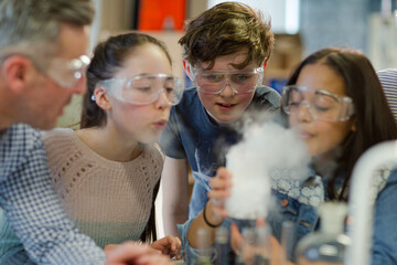 Male teacher and students watching chemical reaction, conducting scientific experiment in laboratory classroom