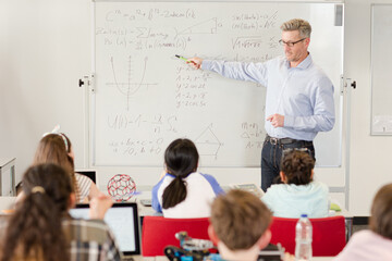 Male teacher leading lesson at whiteboard in classroom
