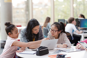 Obraz premium Female teacher and girl students using laptop at table