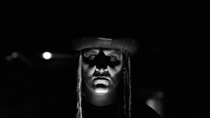 Frightening man face in carnival skull Halloween makeup of skeleton against dark parking hallway....