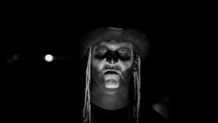 Scary man face in carnival skull Halloween makeup of skeleton against dark parking hallway....