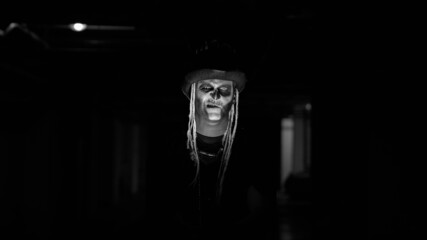 Frightening man in carnival skull Halloween makeup of skeleton against dark parking hallway....