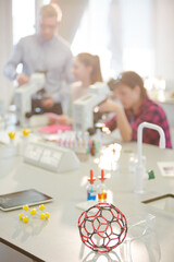 Science teacher helping girl students at microscope in classroom laboratory