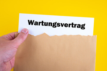 Ein Wartungsvertrag wird aus einem Briefumschlag von einer Hand genommen vor gelben Hintergrund
