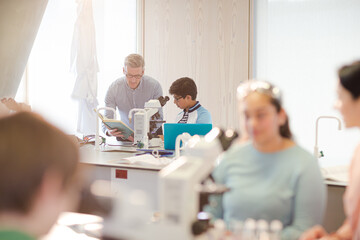 Obraz premium Male teacher and boy student conducting scientific experiment at microscope in laboratory classroom
