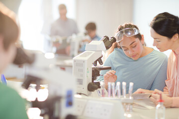 Female teacher and girl student conducting scientific experiment at microscope in laboratory classroom