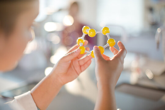 Curious girl student holding molecule model in classroom