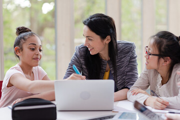 Female teacher and girl students using laptop at table