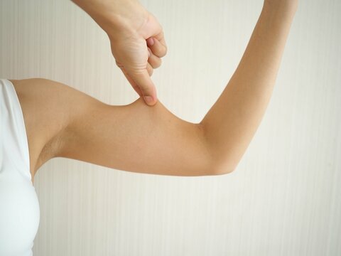 Asian woman pinching loose skin or flab on her upper arm on white background. health care concept. closeup photo, blurred.