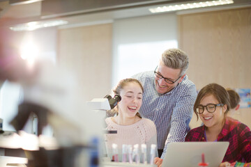 Male teacher helping girl students at microscope in laboratory classroom