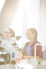 Eager girl students behind microscopes in laboratory classroom