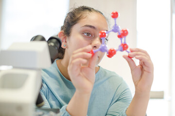 Curious girl student examining molecular structure in laboratory classroom