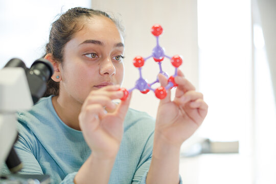 Curious girl student examining molecular structure in laboratory classroom