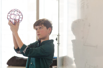 Serious boy student holding molecular structure in classroom