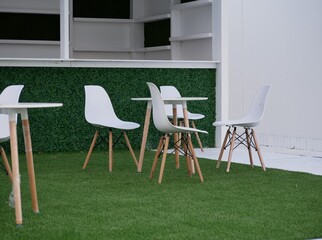 An open-air cafe is preparing to receive guests. New furniture for the cafe is installed, but not unpacked. Furniture made of wood and plastic in white on a green floor.